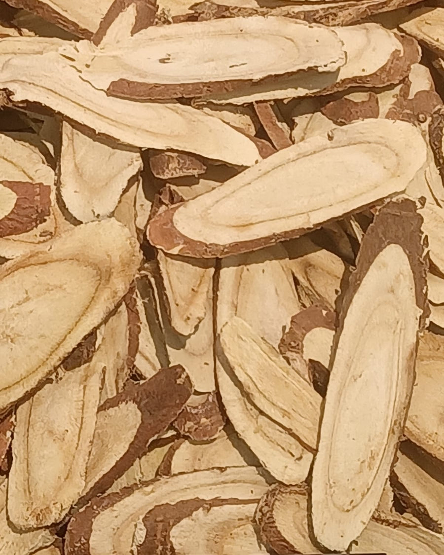 A pile of dried licorice root slices, pale inside with brown bark.